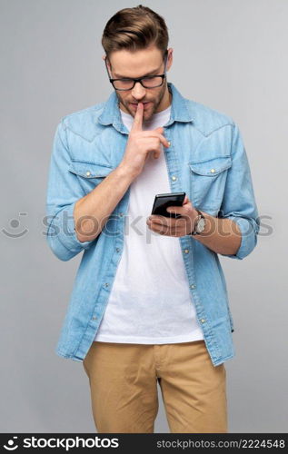 pretty casual man in blue jeans shirt holding his phone standing over studio grey background.. pretty casual man in blue jeans shirt holding his phone standing over studio grey background