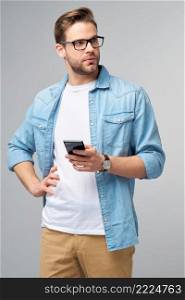 pretty casual man in blue jeans shirt holding his phone standing over studio grey background.. pretty casual man in blue jeans shirt holding his phone standing over studio grey background