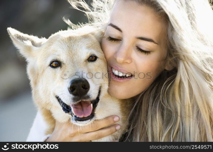 Pretty Caucasian blond woman hugging brown dog and smiling.