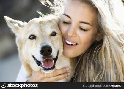 Pretty Caucasian blond woman hugging brown dog and smiling.