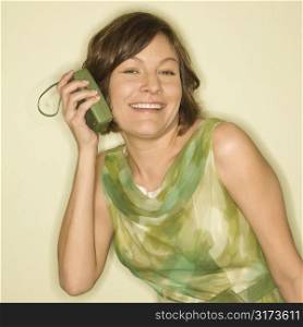 Pretty Caucasian mid-adult woman wearing green vintage dress holding handheld radio up to her ear and smiling at viewer.