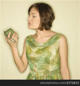 Pretty Caucasian mid-adult woman wearing green vintage dress looking at handheld radio.