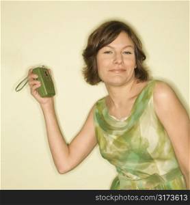 Pretty Caucasian mid-adult woman wearing green vintage dress with handheld radio smiling at viewer.