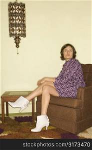 Pretty Caucasian mid-adult woman wearing vintage clothing sitting in brown retro chair looking bored.