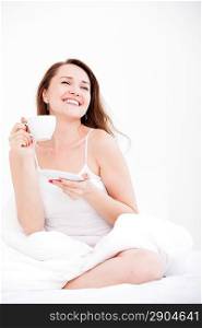 Pretty Caucasian woman sitting on a bed with a cup on a light background