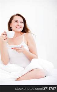 Pretty Caucasian woman sitting on a bed with a cup on a light background