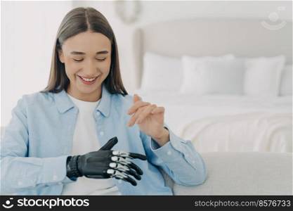 Pretty caucasian woman with artificial arm in bedroom. Happy girl is setting her electronic bionic limb. Smiling woman has modern cyber prosthesis. Engineering and technology concept.. Pretty caucasian woman with artificial arm in bedroom. Engineering and technology concept.