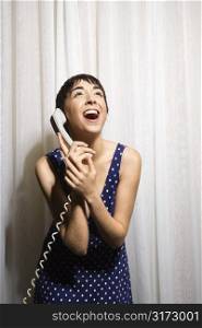 Pretty Caucasian young woman holding telephone receiver to ear and laughing.