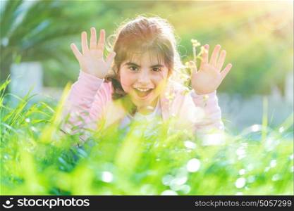 Pretty child playing outdoors, cute little girl raised up hands and laughing, having fun on the fresh green grass field in bright sun light, enjoying nice spring day