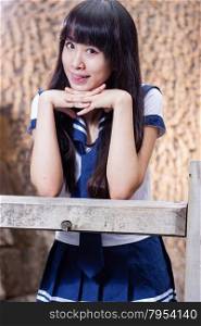 Pretty Chinese high school girl leaning on wooden fence