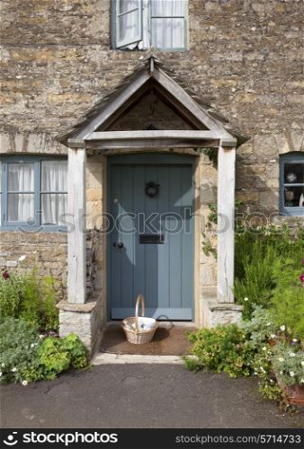 Pretty Cotswold cottage doorway with basket and flowers, Gloucestershire, England.