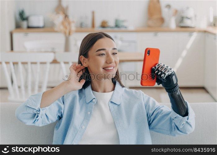 Pretty disabled european woman taking selfie on camera of smartphone. Happy girl is holding the phone with bionic artificial arm. Prosthesis technology. Equality and life quality concept.. Pretty disabled european woman taking selfie on camera of smartphone. Prosthesis technology.