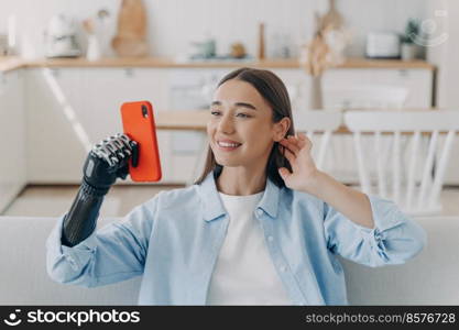 Pretty disabled european woman taking selfie on camera of smartphone. Happy girl is holding the phone with bionic artificial arm. Prosthesis technology. Equality and life quality concept.. Pretty disabled european woman taking selfie on camera of smartphone. Prosthesis technology.