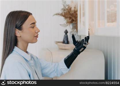 Pretty disabled girl opening kitchen cupboard by bionic prosthetic arm. Young caucasian woman with artificial arm doing chores at home. Advertising of modern prosthesis. Domestic life and disability.. Pretty disabled girl opens kitchen cupboard by bionic prosthetic arm. Modern prosthesis advertising