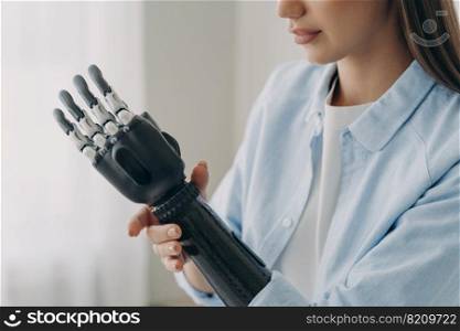 Pretty disabled girl touching her bionic prosthetic arm, close up. Female with robotic hand touches wrist of artificial limb. Medical high tech care for people with disabilities concept.. Disabled girl touches her bionic prosthetic arm. Medical high tech care for people with disabilities