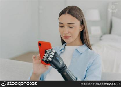 Pretty disabled young girl holding smartphone, using bionic arm prosthesis, chatting with friend in social network. Happy female with disability uses phone apps, shopping in online store.. Happy disabled young girl with bionic arm prosthesis holding smartphone, shopping in online store