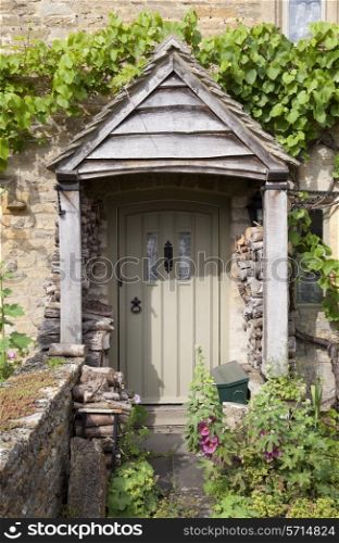 Pretty English cottage doorway with logs and flowers, Cotswolds, Gloucestershire, England.