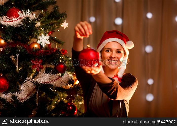 Pretty female near Christmas tree showing Christmas toy&#xA;