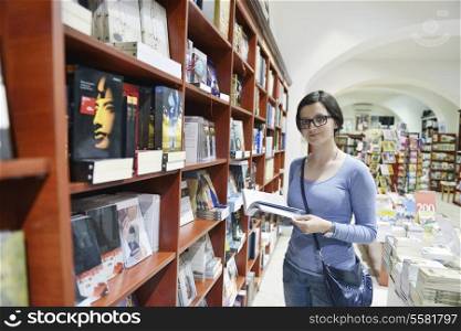 Pretty female student standing at bookshelf in university library store shop searching for a book