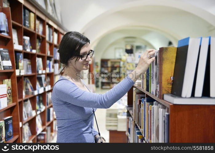 Pretty female student standing at bookshelf in university library store shop searching for a book