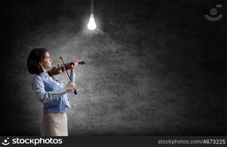 Pretty female violinist. Young woman playing violin and glowing light bulb hanging above
