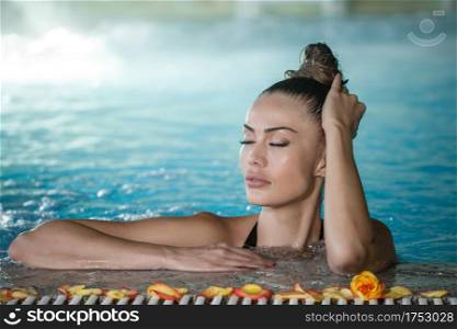 Pretty female with closed eyes touching wet hair while enjoying spa procedure in swimming pool. Sensual woman touching wet hair in pool