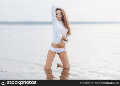 Pretty female with perfect fit body, wears summer clothing, spends spare time at seashore, enjoys wonderful nature view, demonstrates healthy pure skin. Summer vacations and recreation concept