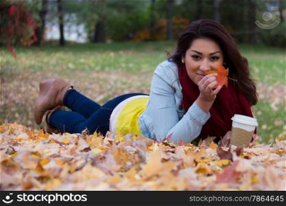 Pretty girl holding up a maple leaf whle lying down on the ground