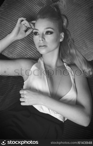 pretty girl , in fashion portrait , she is laying on a sofa i her living room , has blond long hair , and looking wth a dream expression, she is looking up , black and white image