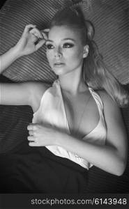 pretty girl , in fashion portrait , she is laying on a sofa i her living room , has blond long hair , and looking wth a dream expression, she is looking up , black and white image