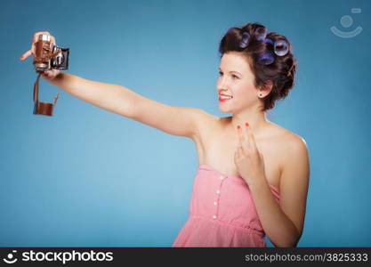 Pretty girl in hair curlers taking picture using vintage camera blue background