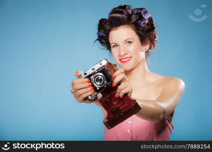 Pretty girl in hair curlers taking picture using vintage camera blue background