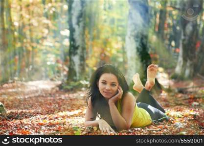 Pretty girl in the autumn forest laying on yellow leaves