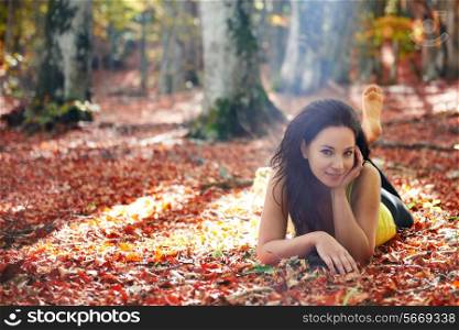 Pretty girl in the autumn forest laying on yellow leaves