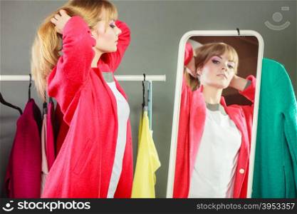 Pretty girl looking into mirror.. Pretty happy woman watching at her into mirror in clothing from new collection wardrobe. Young undecided shopper girl choosing in second hand. Shopping sale concept.