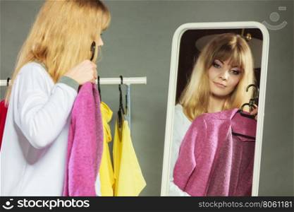 Pretty girl looking into mirror.. Pretty happy woman watching at her into mirror in clothing from new collection wardrobe. Young undecided shopper girl choosing in second hand. Shopping sale concept.