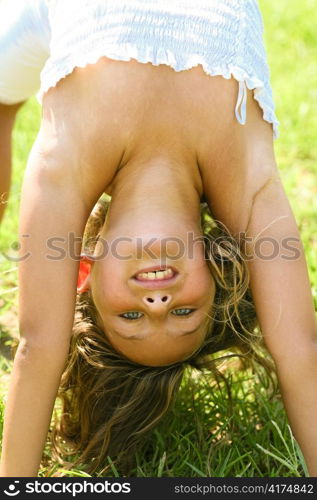 Pretty girl making gymnastic moves on grass looking into camera
