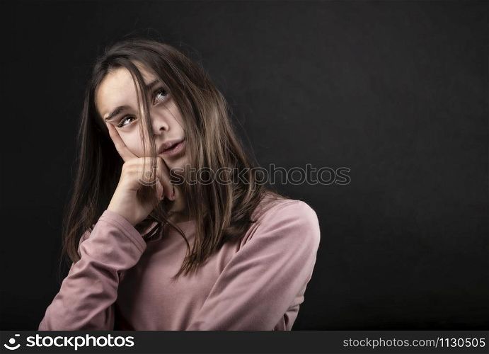 pretty girl posing in a studio with her hands on her face and looking up, against a dark background
