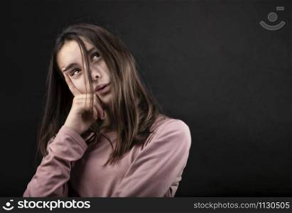 pretty girl posing in a studio with her hands on her face and looking up, against a dark background