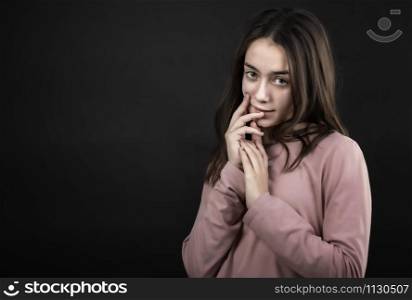 pretty girl posing in the studio with her hands in front of her face, against a dark background