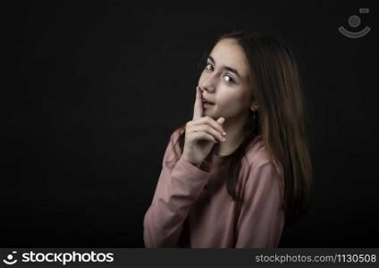 pretty girl posing in the studio with her index finger on her lips, against a dark background