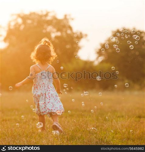Pretty girl runs for the bubbles in the park on the sunset