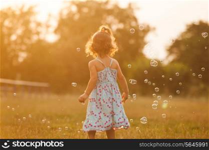 Pretty girl runs for the bubbles in the park on the sunset