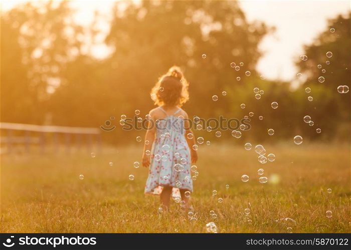 Pretty girl runs for the bubbles in the park on the sunset. Girl and bubbles