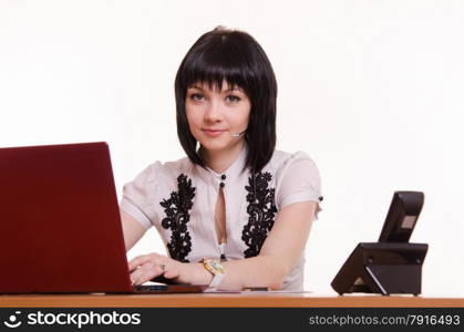Pretty girl sitting in a call center with a laptop in a white blouse with black embroidery. Portrait of a call-center employee in front the monitor