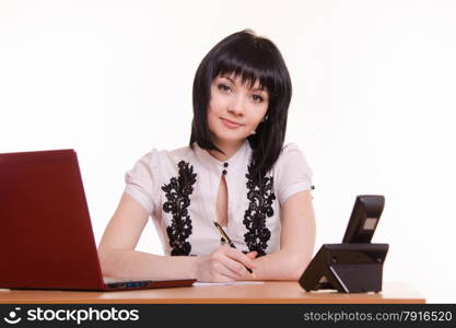 Pretty girl sitting in a call center with a laptop in a white blouse with black embroidery. Office employee call-center with pen in hand