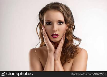 pretty girl with long wavy hair and purple make-up, she looks in to the lens and has both hands on the face