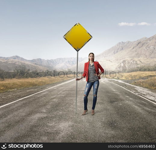 Pretty girl with roadsign. Young woman in red jacket holding yellow road sign