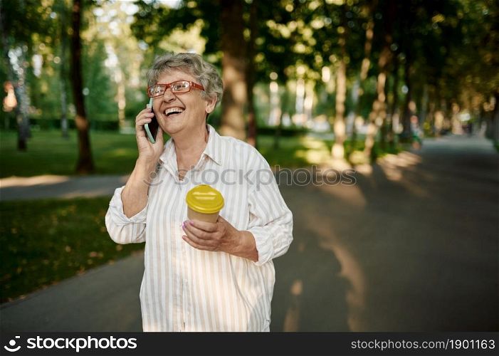 Pretty granny in glasses using mobile phone in summer park. Aged people lifestyle. Funny grandmother having fun outdoors, old female person on nature. Pretty granny using mobile phone in summer park