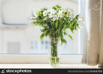 Pretty green flowers bunch in vase at window. Home interior and decoration